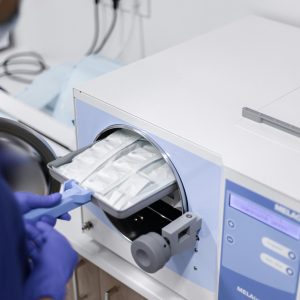 A healthcare worker operates a medical autoclave for sterilizing equipment.